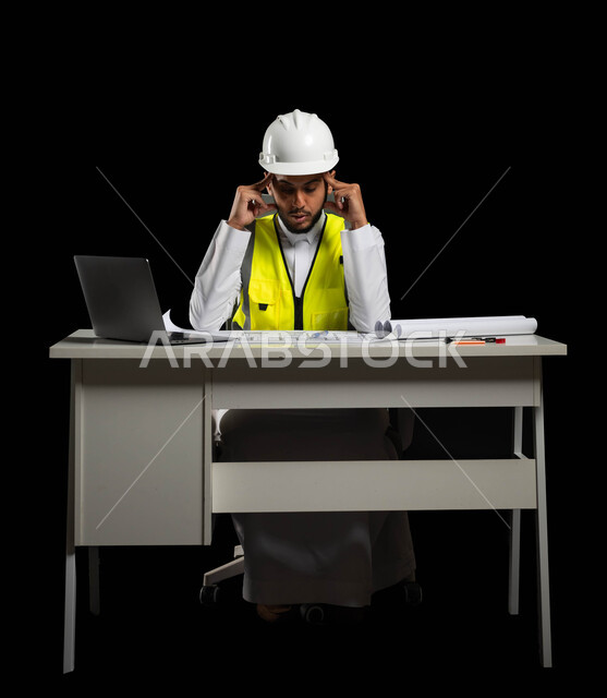 صعوبة متابعة الخطط والتعليمات الهندسية لإكمال العمل, بورتريه لمهندس عربي خليجي سعودي يرتدي الخوذة البيضاء وسترة الحماية الخاصة بالعمل يجلس وراء المكتب ويمسك رأسه بيديه بإيماءات تدل على التعب والإرهاق الشديد، الشعور بالصداع وضرورة التعافي، خلفية سوداء