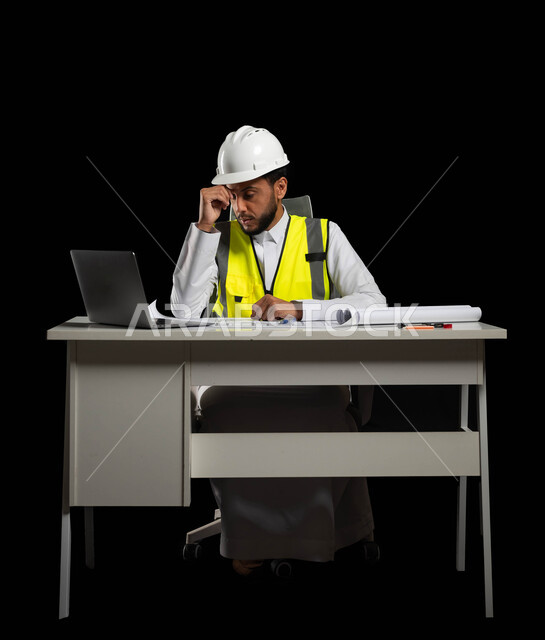 The role of engineers in the Kingdom of Saudi Arabia in the progress of society, hard work and diligence, portrait of a Saudi Arabian Gulf engineer wearing a white helmet and a protective vest, sitting at the desk and placing his hand on his head with gestures indicating fatigue, feeling tired and needing rest, black background.