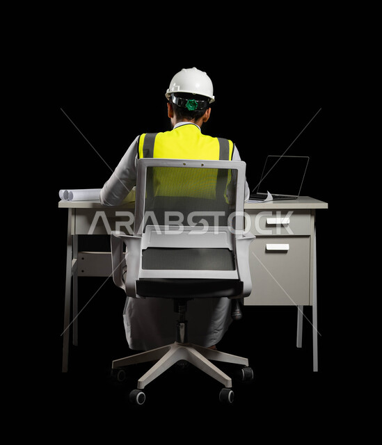 المهن والوظائف الهندسية السعودية, مفهوم الهندسة الإنشائية والمعمارية ،بورتريه من الخلف لمهندس عربي خليجي سعودي يرتدي الخوذة البيضاء وسترة العمل الخاصة يجلس على الكرسي وأمامه المكتب, جهاز الحاسوب المحمول وبعض المخططات المعمارية على الطاولة الهندسية, خلفية سوداء