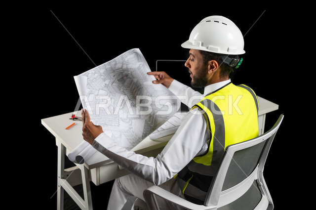 الاهتمام بالتطور العمراني بسواعد المهندسين السعوديين, دور الهندسة الإنشائية في تطور المجتمع السعودي, بورتريه لمهندس عربي خليجي سعودي يرتدي خوذة الحماية والسترة الخاصة بالعمل يجلس على المكتب,عرض مخطط البناء بشكل كامل، الإشراف على سير العمل, خلفية سوداء
