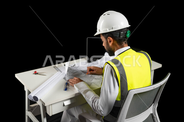 دعم وتنمية القطاع الهندسي في المملكة العربية السعودية, مفهوم الهندسة والإنشاءات المعمارية، بورتريه لمهندس عربي خليجي سعودي يرتدي الخوذة البيضاء والسترة الخاصة بالعمل يجلس على المكتب ويمسك بيده القلم ويرسم المخطط الهندسي ، إكمال رسم مخطوطات البناء، خلفية سوداء