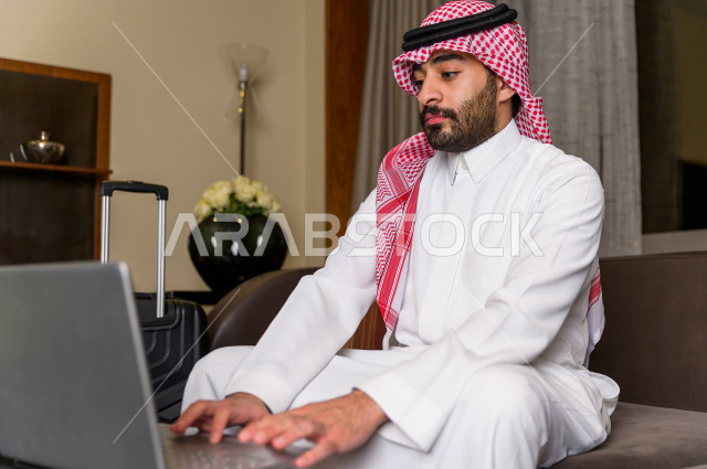 رجل خليجي سعودي يسافر بداعي العمل وينزل في أحد الفنادق , رجل أعمال خليجي يحمل معه حقيبة السفر و الأجهزة الذكية للعمل في الفندق , سياحة وسفر , شاب سعودي يكتب بعض الملاحظات عن اقامته في الفندق , حب الاستطلاع والشغف في العمل . 