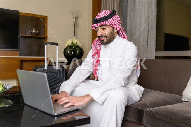 رجل خليجي سعودي يسافر بداعي العمل وينزل في أحد الفنادق , رجل أعمال خليجي يحمل معه حقيبة السفر و الأجهزة الذكية للعمل في الفندق , سياحة وسفر , شاب سعودي يكتب بعض الملاحظات عن اقامته في الفندق , حب الاستطلاع والشغف في العمل . 