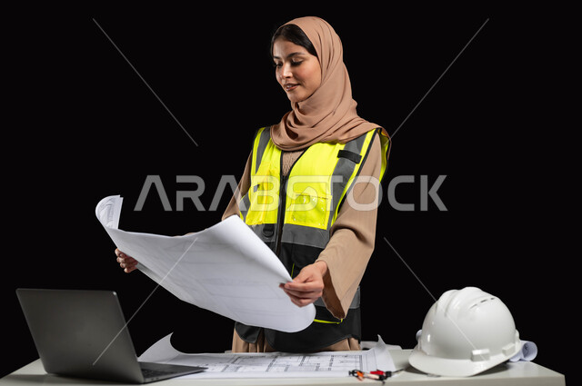 Engineering designs and checking plans, working in the engineering field, a close-up portrait from the side of a veiled Saudi Arabian Gulf engineer wearing a protection vest and helmet holding the reconstruction plan, engineering project management, women’s professions and jobs, black background, sensitive content, sensitive use