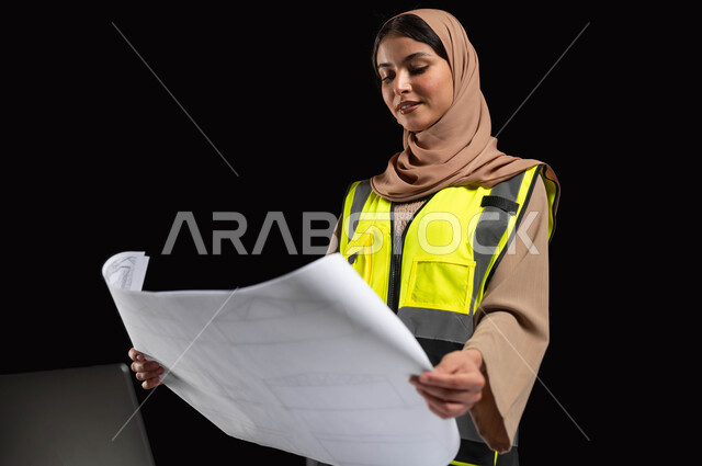 The role of structural engineering in the development of Saudi society, architectural designs and checking plans, a close-up portrait of a veiled Saudi Gulf Arab engineer wearing a protection jacket and helmet looking at the reconstruction plan with gestures of pride and joy, women’s professions and jobs, black background, sensitive content, sensitive use