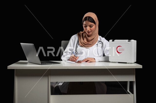 استخدام جهاز الحاسوب المحمول وحقيبة الاسعافات الأولية، بورتريه مقرب لطبيبة عربية خليجية ترتدي المعطف الأبيض تقوم بكتابة وتدوين التقارير والحالات الصحية، دمج العمل الطبي مع التكنولوجيا، خلفية سوداء, محتوى حساس, استخدام حساس