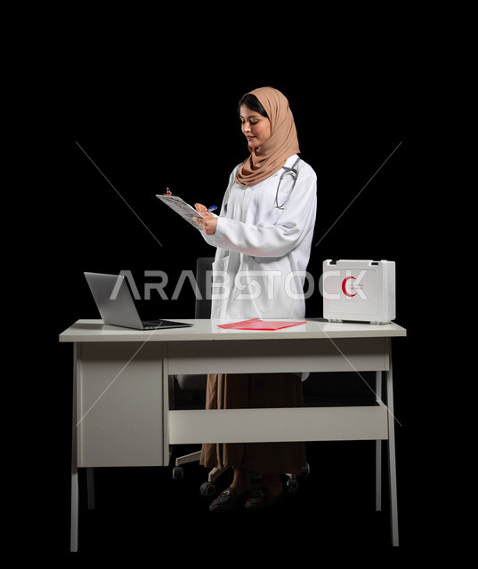 مهن ووظائف نسائية سعودية، استخدام حقيبة الاسعافات الاوليه والحاسوب المحمول في مجال الطب, بورتريه لطبيبة عربية خليجية ترتدي المعطف الأبيض تقوم بكتابة وتدوين التقارير والحالات الصحيه، الجسم بالطول الكامل، خلفية سوداء, محتوى حساس, استخدام حساس