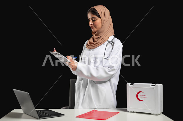 Working in the medical sector and supervising patients in the Kingdom of Saudi Arabia, a close-up portrait of a Saudi Gulf Arab doctor wearing a medical coat reviewing a medical report on a medical condition from the computer, integrating work with technology, sensitive use, sensitive content