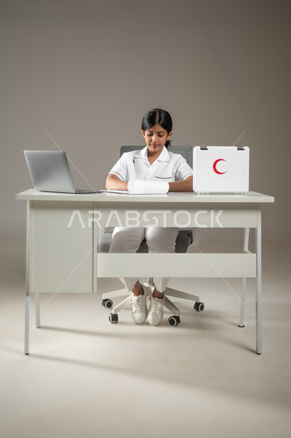 استعمال التكنولوجيا الحديثة في المجال الطبي، حقيبة الإسعافات الأولية، بورتريه لطفلة عربية سعودية خليجية ترتدي زي الممرضة تقوم بتدوين ملاحظات المرضى، مهن ووظائف مستقبلية، صورة لكامل الجسم، خلفية رمادية، محتوى حساس، استخدام حساس