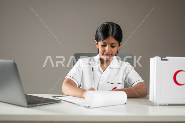 دمج التكنولوجيا الحديثة في المجال الطبي، حقيبة الإسعافات الأولية، بورتريه مقرب لطفلة عربية سعودية خليجية ترتدي زي الممرضة تقوم بتدوين ملاحظات المرضى، مهن ووظائف مستقبلية، خلفية رمادية، محتوى حساس، استخدام حساس