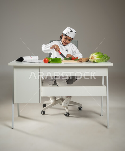 تذوق الطعام من أيدي الشيف الصغيرة,نحضير وتقديم الأطباق اللذيذة, بورتريه لطفلة عربية خليجيه سعودية ترتدي زي الطباخ الخاص تقطع الخضروات بكل مهارة, إيماءات السعادة والفرح، تشجيع المواهب منذ مرحلة الطفولة, خلفية رمادية, محتوى حساس