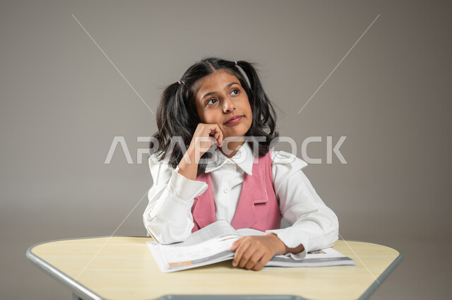 التأمل بعيون حالمة للوصول إلى الهدف, الجد والاجتهاد في المذاكرة, حب التعلم والمطالعة واكتشاف معلومات جديدة, بورتريه لتلميذة عربية خليجية سعودية تجلس في مقعدها وتنظر في الافق الواسع, خلفية رمادية, محتوى حساس