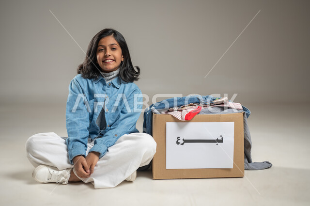 خدمة المجتمع السعودي المتعفف, إهداء ملابس العيد للمحتاجين, جمعيات خيرية ومبادرات انسانية، بورتريه بخلفية رمادية لطفلة عربية خليجية سعودية ترتدي زي كاجوال لطيف تنظر إلى الكاميرا بعيون يملؤها الامتنان, مبادرات تطوعية خيرية, محتوى حساس