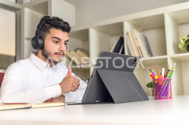 شاب سعودي خليجي يدرس في المنزل باستخدام جهاز التابلت، يتابع حصص الاونلاين ، التعلم عن بعد ، مفهوم التعليم عبر الانترنت ،الدراسة من خلال منصة تعليمية للتعلم عن بعد  ، العزلة الذاتية .