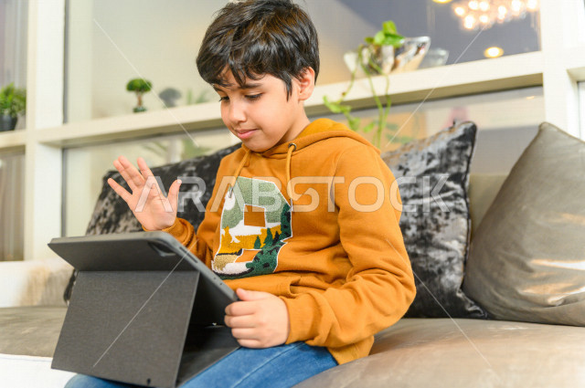 تلميذ سعودي خليجي يدرس في المنزل باستخدام جهاز التابلت ، يتابع حصص الاونلاين عن طريق الحاسوب المحمول ، الدراسة من خلال منصة تعليمية للتعلم عن بعد ، التعلم عن بعد ، مفهوم التعليم عبر الانترنت ، كورونا ، العزلة الذاتية .