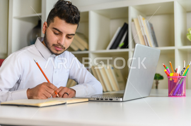 شاب سعودي خليجي يدرس في المنزل باستخدام جهاز التابلت، يتابع حصص الاونلاين ، التعلم عن بعد ، مفهوم التعليم عبر الانترنت ،الدراسة من خلال منصة تعليمية للتعلم عن بعد  ، العزلة الذاتية .
