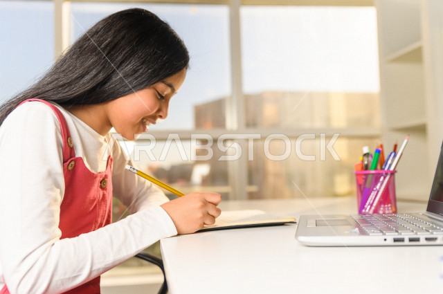 A Saudi Arabian student studying at home and using a laptop, studying through an educational platform for distance learning, performing homework, distance learning, the concept of online education, home education, self-isolation.