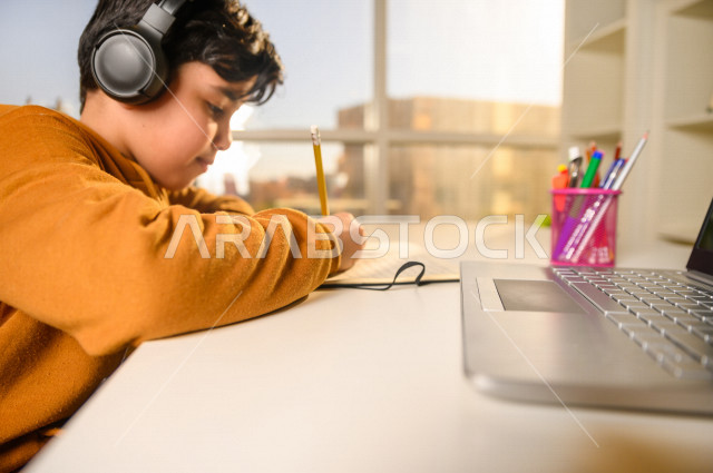 تلميذ سعودي خليجي يدرس في المنزل باستخدام جهاز التابلت ، يتابع حصص الاونلاين عن طريق الحاسوب المحمول ، الدراسة من خلال منصة تعليمية للتعلم عن بعد ، التعلم عن بعد ، مفهوم التعليم عبر الانترنت ، كورونا ، العزلة الذاتية .