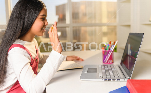 تلميذة سعودية خليجية تدرس في المنزل وتستخدم الحاسوب المحمول ،الدراسة من خلال منصة تعليمية للتعلم عن بعد ، تأدية الواجبات المدرسية ،  التعلم عن بعد ، مفهوم التعليم عبر الانترنت ، التعليم المنزلي ، العزلة الذاتية .