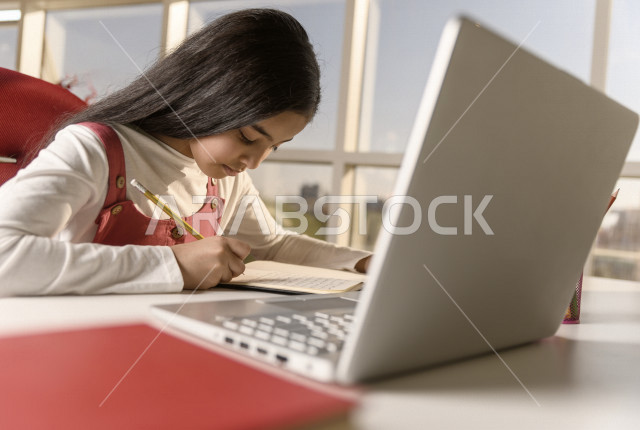 تلميذة سعودية خليجية تدرس في المنزل وتستخدم الحاسوب المحمول ،الدراسة من خلال منصة تعليمية للتعلم عن بعد ، تأدية الواجبات المدرسية ،  التعلم عن بعد ، مفهوم التعليم عبر الانترنت ، التعليم المنزلي ، العزلة الذاتية .