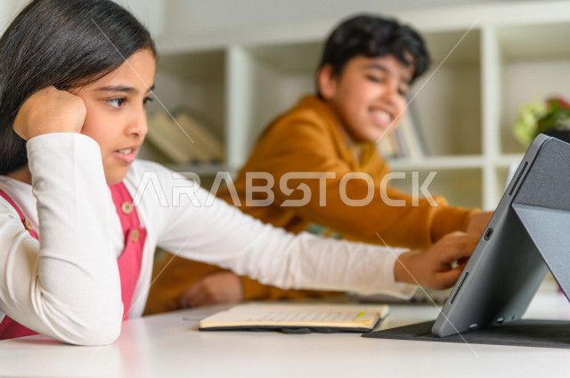 A brother and sister of two Saudi Arabian Gulf students share a homework solution through the tablet, studying through an educational platform for distance learning, distance learning, the concept of online education, home education, and self-isolation.