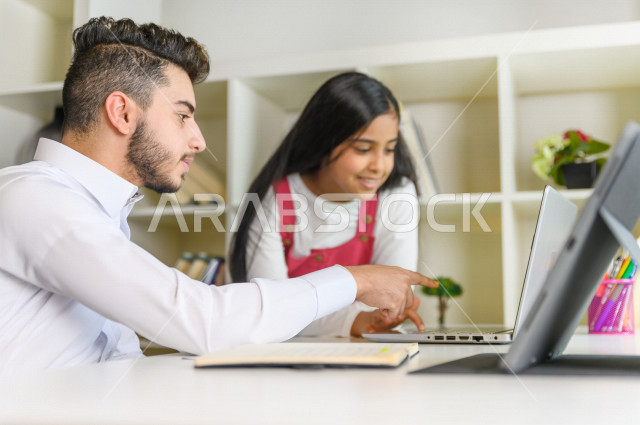 تلميذ سعودي خليجي يقوم بتشجيع اخته الصغيرة على تأدية واجباتها ،  يتشاركان في حل الواجب المنزلي من خلال الأجهزة التقنية ،الدراسة من خلال منصة تعليمية للتعلم عن بعد ،  التعلم عن بعد ، مفهوم التعليم عبر الانترنت ، التعليم المنزلي ، العزلة الذاتية .