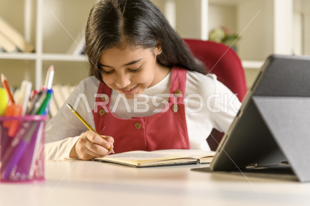 تلميذة سعودية خليجية تدرس في المنزل وتستخدم الحاسوب المحمول ،الدراسة من خلال منصة تعليمية للتعلم عن بعد ، تأدية الواجبات المدرسية ،  التعلم عن بعد ، مفهوم التعليم عبر الانترنت ، التعليم المنزلي ، العزلة الذاتية .