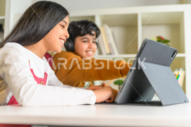 Brother and sister of two Saudi Gulf students studying at home with the help of technical devices, studying through an educational platform for distance learning, doing homework, distance learning, the concept of online education, home education, self-iso