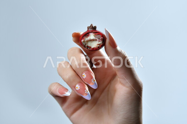 تذوق قطعة من الحلا، أنواع  الشوكولاته الفاخرة، تقديم الحلويات والسكريات في الأعياد والمناسبات، صورة مقربة ليد امرأة عربية تمسك بقطعة من الشوكولا، خلفية رمادية