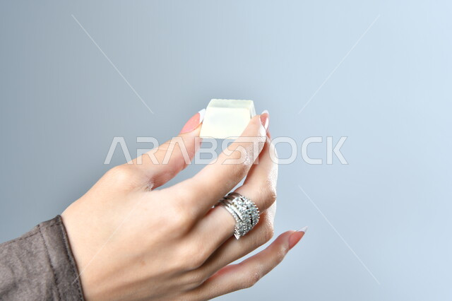 الشوكولاته البيضاء الفاخرة بأشكال فنية مختلفة، تقديم الحلويات في الأعياد والمناسبات، صورة مقربة ليد امرأة عربية تمسك بقطعة من الشوكولا، خلفية رمادية