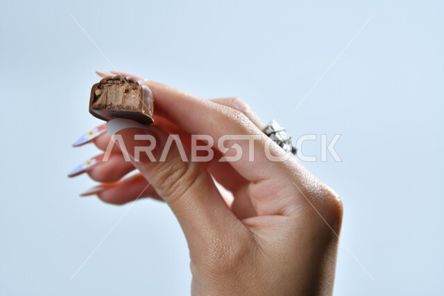 تذوق حبات الشوكولاته الفاخرة، تقديم الحلويات والسكريات في الأعياد والمناسبات، صورة مقربة ليد امرأة عربية تمسك بقطعة من الشوكولا، خلفية رمادية