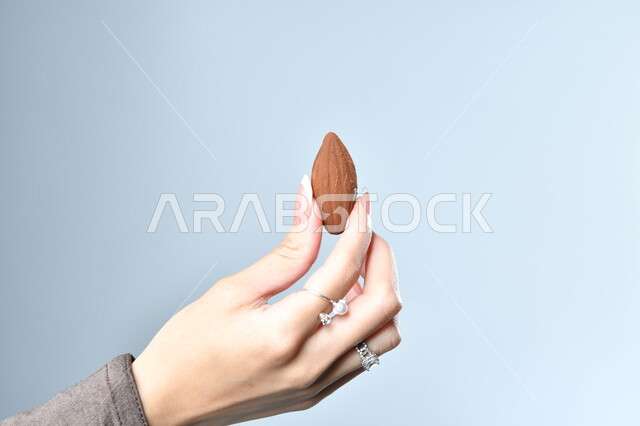 حبات الشوكولاته الفاخرة بأشكال فنية مختلفة، تقديم الحلويات في الأعياد والمناسبات، صورة مقربة ليد امرأة عربية تمسك بقطعة من الشوكولا، خلفية رمادية