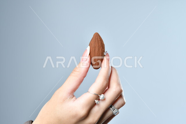 الأشكال الفنية المختلفة لحبات الشوكولاته الفاخرة، تقديم الحلويات في الأعياد والمناسبات، صورة مقربة ليد امرأة عربية تمسك بقطعة من الشوكولا، خلفية رمادية
