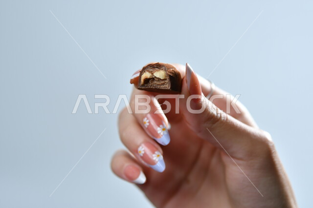 تذوق حبات الشوكولاته الفاخرة، تقديم الحلويات والسكريات في الأعياد والمناسبات، صورة مقربة ليد امرأة عربية تمسك بقطعة من الشوكولا، خلفية رمادية