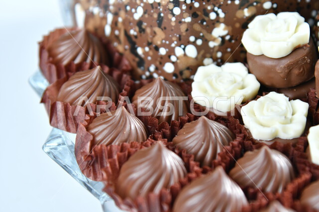 حلوى العيد اللذيذة، صورة مقربة لمجموعة من حبات الشوكولاته الفاخرة بأشكال فنية مختلفة، تقديم الحلويات والسكريات في الأعياد والمناسبات، كرم الضيافة العربية، خلفيه بيضاء