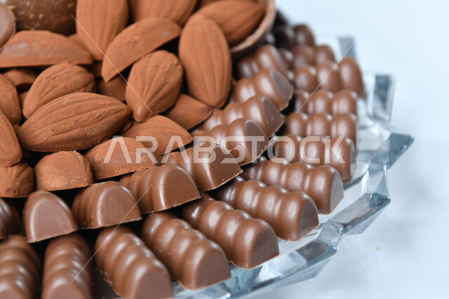 طبق يحوي مجموعة من حبات الشوكولاته الفاخرة بأشكال فنية مختلفة، كرم الضيافة العربية، حلوى العيد اللذيذة، تقديم الحلويات والسكريات في الأعياد والمناسبات، خلفيه بيضاء