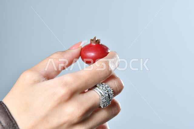 حبات الشوكولاته الفاخرة بأشكال فنية مختلفة، تقديم الحلويات في الأعياد والمناسبات، صورة مقربة ليد امرأة عربية تمسك بقطعة من الشوكولا، خلفية رمادية