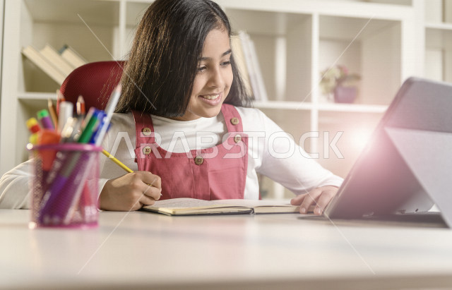 A Saudi Arabian student studying at home and using a laptop, studying through an educational platform for distance learning, performing homework, performing homework, distance learning, the concept of online education, homeschooling, self-isolation.