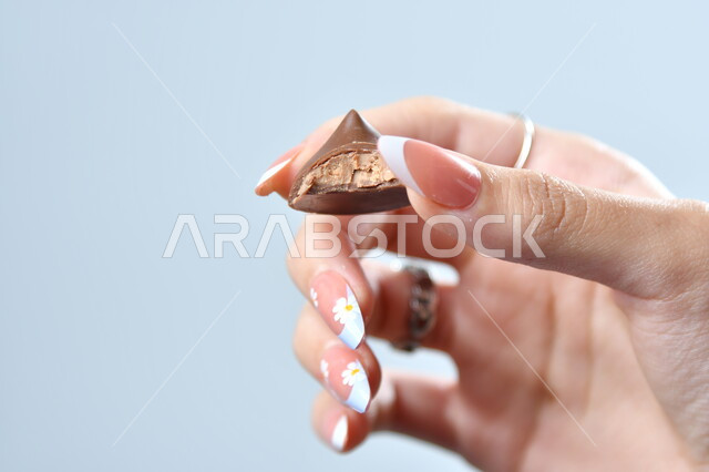 تذوق حبات الشوكولاته الفاخرة، تقديم الحلويات والسكريات في الأعياد والمناسبات، صورة مقربة ليد امرأة عربية تمسك بقطعة من الشوكولا، خلفية رمادية