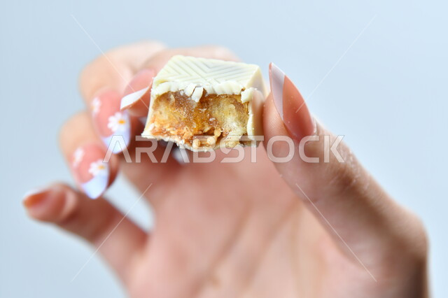 الأنواع المختلفة للشوكولاته الفاخرة، تقديم الحلويات والسكريات في الأعياد والمناسبات، صورة مقربة ليد امرأة عربية تمسك بقطعة من الشوكولا، تذوق قطعة من الحلا، خلفية رمادية