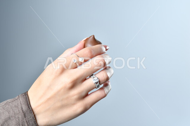 تناول الحلويات والسكريات، الأشكال الفنية المختلفة لحبات الشوكولاته الفاخرة، صورة مقربة ليد امرأة عربية تمسك بقطعة من الشوكولا، خلفية رمادية