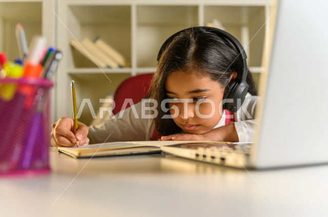 تلميذة سعودية خليجية تقوم بحل الواجبات في المنزل ،الدراسة من خلال منصة تعليمية للتعلم عن بعد ، تأدية الواجبات المدرسية ، ايماءات وجه تدل على التفكير، التعلم عن بعد ، مفهوم التعليم عبر الانترنت ، التعليم المنزلي ، العزلة الذاتية .