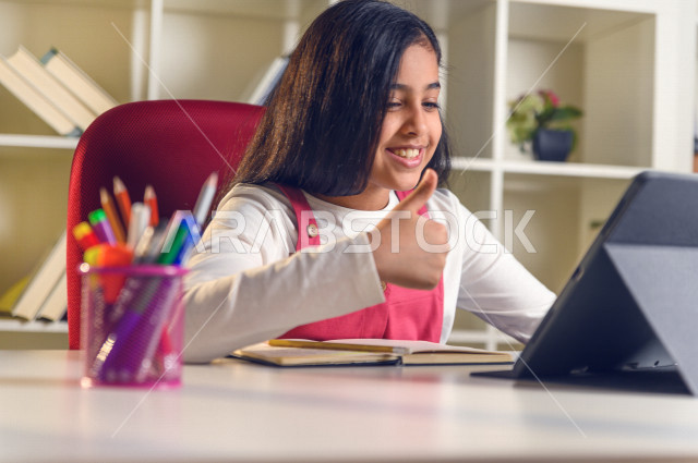A Saudi Arabian student studying at home and using a laptop, raising a thumb, studying through an educational platform for distance learning, doing schoolwork, performing homework, distance learning, the concept of online education, home education, self-i