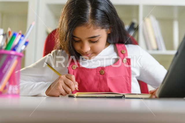 تلميذة سعودية خليجية تقوم بحل الواجبات في المنزل ،الدراسة من خلال منصة تعليمية للتعلم عن بعد ، تأدية الواجبات المدرسية ، ايماءات وجه تدل على التفكير، التعلم عن بعد ، مفهوم التعليم عبر الانترنت ، التعليم المنزلي ، العزلة الذاتية .