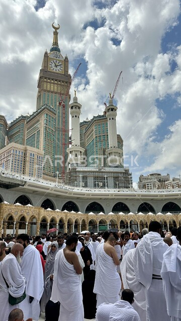 اطلالة برج الساعة من باحة المسجد الحرام في مكة المكرمة ، أداء مناسك الحج والعمرة، العبادة والتقرب إلى الله تعالى، الحجاج والمعتمرين في ساحة الحرم المكي الشريف، الفن الهندسي المعماري للمعالم الإسلامية المقدسة
