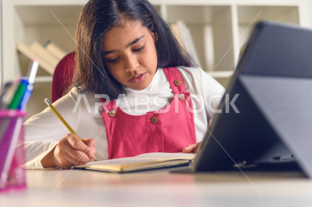 تلميذة سعودية خليجية تقوم بحل الواجبات في المنزل ،الدراسة من خلال منصة تعليمية للتعلم عن بعد ، تأدية الواجبات المدرسية ، ايماءات وجه تدل على التفكير، التعلم عن بعد ، مفهوم التعليم عبر الانترنت ، التعليم المنزلي ، العزلة الذاتية .