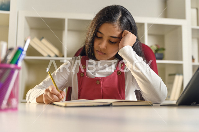 تلميذة سعودية خليجية تقوم بحل الواجبات في المنزل ،الدراسة من خلال منصة تعليمية للتعلم عن بعد ، تأدية الواجبات المدرسية ، ايماءات وجه تدل على التفكير، التعلم عن بعد ، مفهوم التعليم عبر الانترنت ، التعليم المنزلي ، العزلة الذاتية .