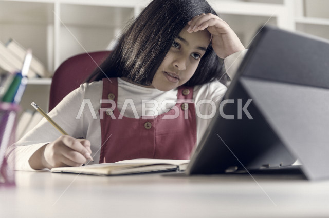 تلميذة سعودية خليجية تقوم بحل الواجبات في المنزل ،الدراسة من خلال منصة تعليمية للتعلم عن بعد ، تأدية الواجبات المدرسية ، ايماءات وجه تدل على التفكير، التعلم عن بعد ، مفهوم التعليم عبر الانترنت ، التعليم المنزلي ، العزلة الذاتية .