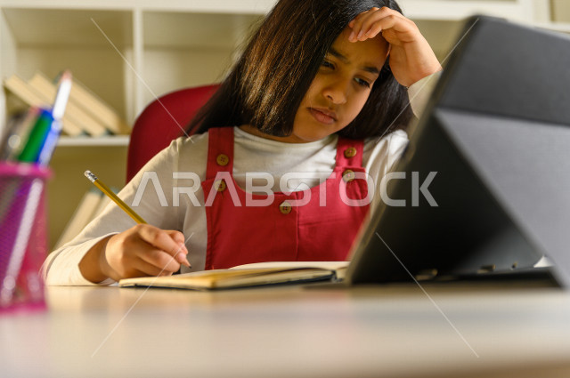 تلميذة سعودية خليجية تقوم بحل الواجبات في المنزل ،الدراسة من خلال منصة تعليمية للتعلم عن بعد ، تأدية الواجبات المدرسية ، ايماءات وجه تدل على التفكير، التعلم عن بعد ، مفهوم التعليم عبر الانترنت ، التعليم المنزلي ، العزلة الذاتية .