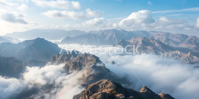 الوديان والقمم الصخرية في البراري، منظر الغيوم والسحب البيضاء في السماء تخترق سلسلة الجبال والتكوينات والتشكلات الصخرية في المناطق الصحراوية، اماكن سياحية مشهورة في المملكة العربية السعودية